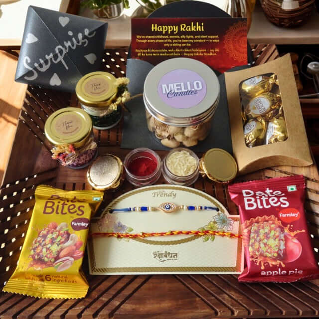 Gifting arrangement with Rakhi, candles, and snacks on a wooden surface