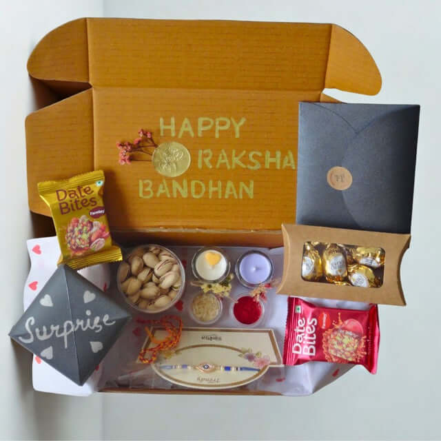 Gift box with Raksha Bandhan-themed items including snacks and a card on a white background