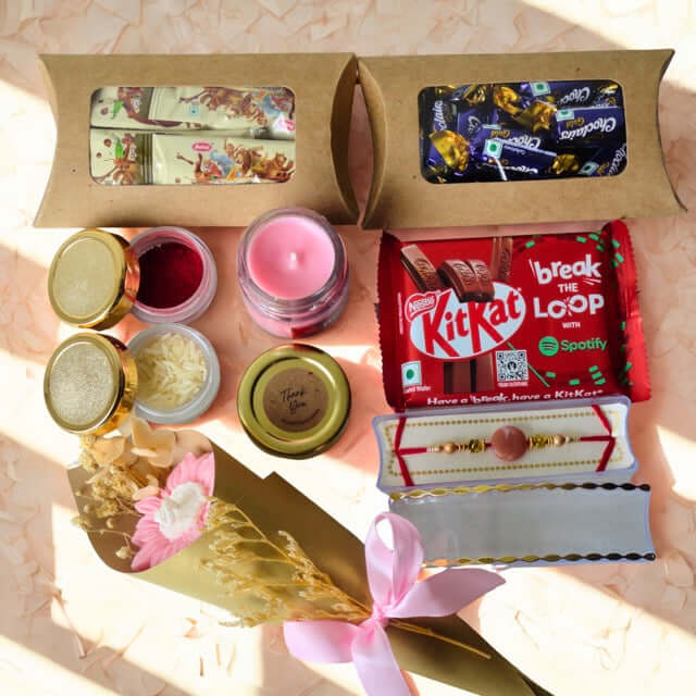 Gift box with KitKat, candles, and a Rakhi on a light pink background