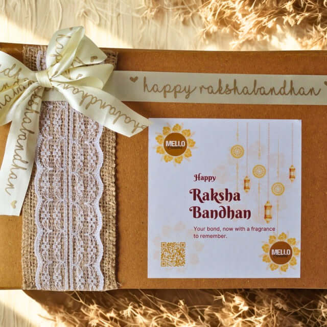 Gift box with lace ribbon and 'Happy Raksha Bandhan' card on a textured surface