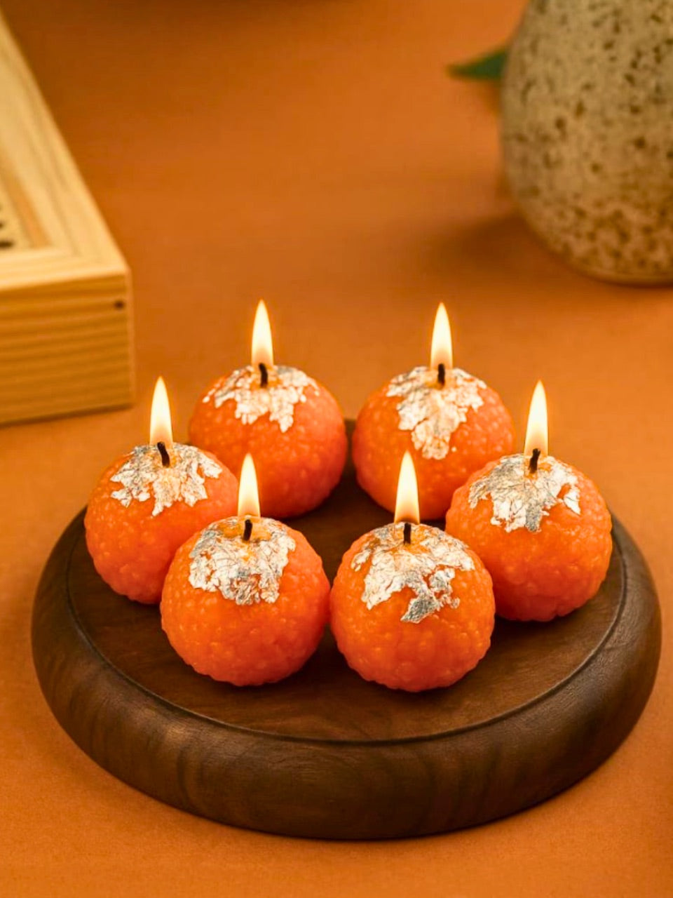 Set of orange candles with silver snowflake decorations on a wooden holder against an orange background.
