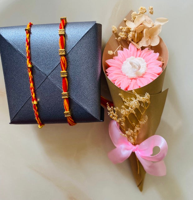 Rakhi with red and gold braided design next to a bouquet of candle flowers on a light background