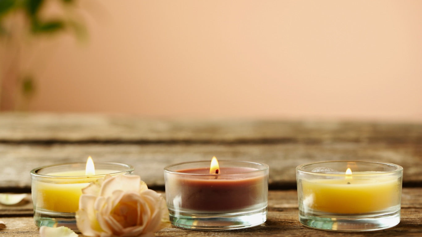 Three small candles in glass holders on a wooden surface with a blurred background