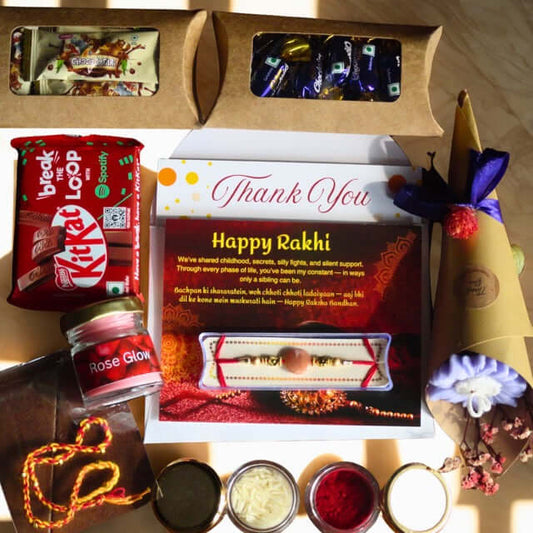 Gift box with Rakhi items including KitKat, Rose Glow, and a card with 'Happy Rakhi' text.
