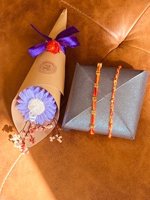 Bouquet of candle flowers in a decorative paper wrap next to two Rakhis