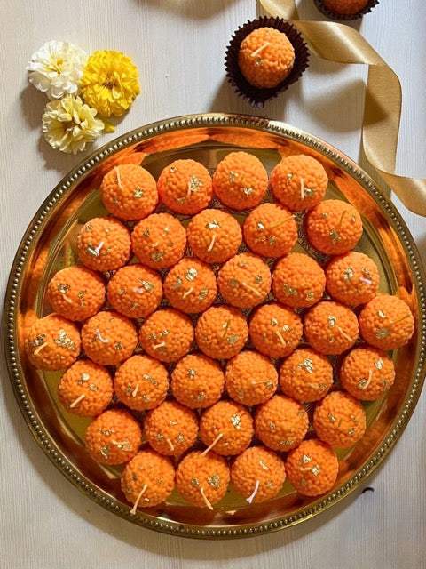 Ornate platter of orange laddus with decorative flowers on a light background