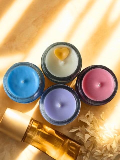 Four small candles in different colors on a textured surface with a warm glow.